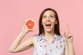 Excited young woman looking, pointing index finger up holding half of fresh ripe grapefruit isolated on pink pastel wall Royalty Free Stock Photo