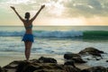 Excited young woman raising arms at the beach in front of the ocean. View from back. Sunset at the beach. Bali, Indonesia Royalty Free Stock Photo