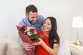 Excited young woman receiving unexpected Bouquet of red roses from husband at home, loving generous boyfriend making romantic