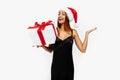 Excited young woman in red Santa Claus hat and black elegant dress, with gift on white background, holiday concept, New Year, Royalty Free Stock Photo