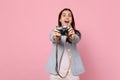 Excited young woman in striped jacket keeping mouth open taking pictures on retro vintage photo camera isolated on pink Royalty Free Stock Photo