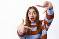 Excited young woman taking picture with finger frames camera gesture, making shot, standing against white background Royalty Free Stock Photo