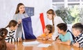 Excited young woman teacher showing national flag of France and telling preteens schoolchildren history of country