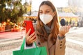 Excited young woman wearing medical mask FFP2 KN95 watching smartphone and holding shopping bags walking in the Christmas Markets Royalty Free Stock Photo