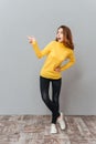 Excited young woman in yellow sweater standing and pointing away Royalty Free Stock Photo