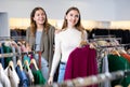 Excited young women holding autumn clothes on racks and choosing season outfit in a shopping mall