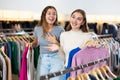 Happy young women holding winter jumpers and sweaters on racks during shopping in a boutique