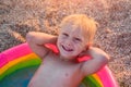 Exciting fair-haired boy in bright inflatable pool, sandy beach. Happy childhood concept