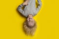 Exciting fair-haired boy hanging upside down on yellow background