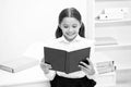 Exciting literature concept. Girl child read book stand white interior. Schoolgirl studying textbook. Kid girl school