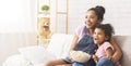 Two emotional african sisters watching tv and eating popcorn