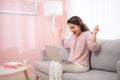 Exciting young Asian woman using laptop when sitting on sofa at home Royalty Free Stock Photo
