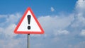 Exclamation mark on a road sign with a white nameplate background sky with clouds