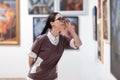 Excursion at galleryexhibition. Side view of caucasian pretty young woman wearing glasses contemplates arts. Defocused Royalty Free Stock Photo