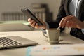 Executive hands stirring coffee checking phone at night