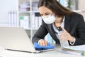 Executive with mask cleaning laptop with sanitizer