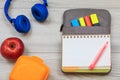 Exercise book on bag-pencil case with color felt pens and marker, sandwich box, apple and headphones on grey background Royalty Free Stock Photo