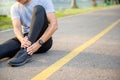 Exercise Injury Concept: A young Asian runner sits down on a park street due to pain in his ankle and grabs his sore ankle and