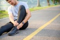 Exercise Injury Concept: A young Asian runner sits down on a park street due to pain in his ankle and grabs his sore ankle and