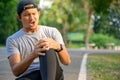 Exercise Injury Concept: A young Asian runner sits down on a park street due to pain in his knee and uses a hand to grasp the sore