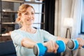 Positive adult lady raising heavy dumbbells while having training at home Royalty Free Stock Photo