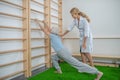 Elderly woman doing lunging near a wall-mounted ladder with instructor