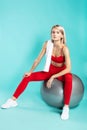 Exercising with fitness ball. Young beautiful blonde woman in sportswear with towel on shoulder sitting on fitness ball Royalty Free Stock Photo