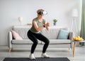 Exercising with virtual reality concept. Athletic mature woman in VR headset doing squats on her home workout
