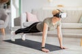 Exercising with virtual reality concept. Mature woman in VR headset standing in plank pose at home