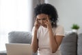 Exhausted African American woman massaging temples, using laptop