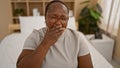 Exhausted african american woman sitting on cozy bed, yawning a heavy morning yawn in a relaxed bedroom atmosphere, conveying the Royalty Free Stock Photo