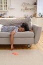 Exhausted African American woman sleeping on couch at home, dropping cellphone on the floor. Fatigue