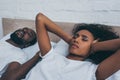 African american woman covering ears with hands while lying near snoring husband
