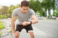 Exhausted asian male athlete hands on knee, checking his heart rate on smartwatch