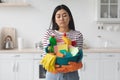 Exhausted asian woman with cleaning tools standing at kitchen