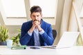 Exhausted businessman sitting at desk behind his laptop at office desk Royalty Free Stock Photo