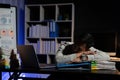 Exhausted businessman sleeping at his desk and working overtime late at night, he is surrounded by piles of paperwork Royalty Free Stock Photo