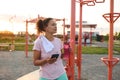 Motivated athletic woman drinking water and checking mobile fitness app on her smartphone while resting after hard workout at