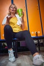 Exhausted elderly senior woman sitting on bench in gym dressing room relaxing and drinking water after workout Royalty Free Stock Photo