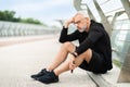 Exhausted elderly sportsman sitting on ground, working out outdoor