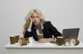 Exhausted female office worker surrounded by empty coffee cups sleeping at workplace over light grey studio background