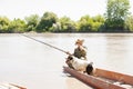 Exhausted male angler with dog, wiping sweat from forehead, while sitting in boat and fishing.