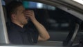 Exhausted male police officer sitting in car, suffering headache, hard day