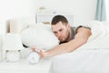 Exhausted man switching off his alarm clock