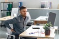 Exhausted mature businessman having acute back pain, massaging aching muscles while sitting at desk in office