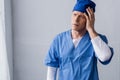 Exhausted and middle aged doctor in blue scrub hat touching head