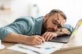 Exhausted millennial man sleeping on his office desk, next to laptop and documents, tired of overworking Royalty Free Stock Photo