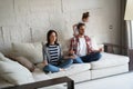 Exhausted mother and father sitting on couch feels annoyed tired while noisy little daughter shouting run around sofa.