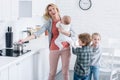 exhausted mother with infant kid cooking and looking up while naughty children playing