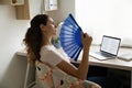 Exhausted overheated woman waving fan, sitting at work desk